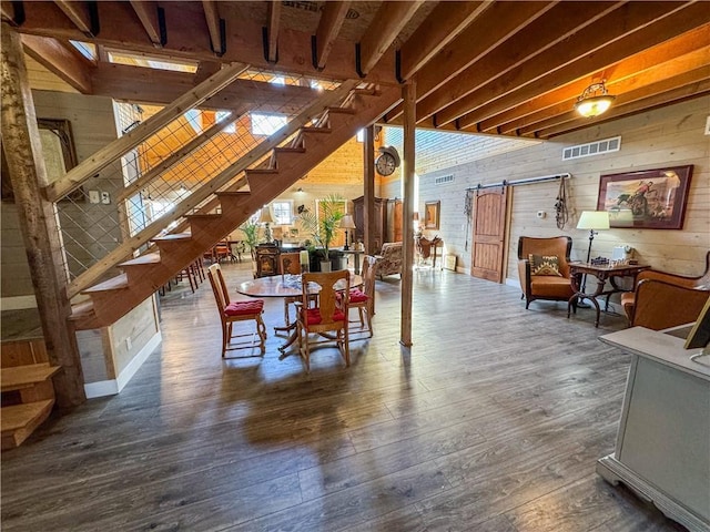 dining room with a barn door, wood walls, wood finished floors, visible vents, and stairs