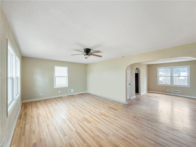 spare room with arched walkways, visible vents, light wood-style flooring, and baseboards