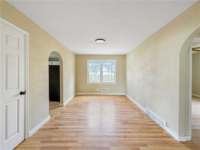 spare room with visible vents, arched walkways, and light wood finished floors