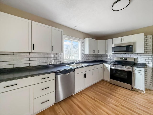 kitchen with dark countertops, light wood-style flooring, appliances with stainless steel finishes, and a sink