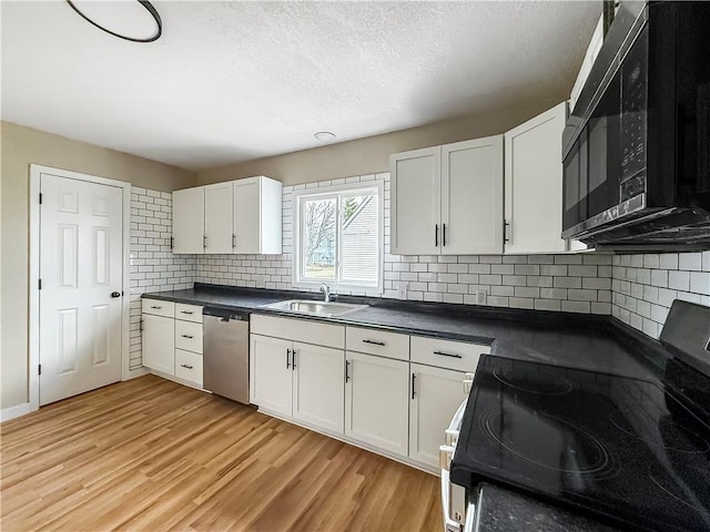 kitchen with a sink, white cabinets, appliances with stainless steel finishes, dark countertops, and light wood-type flooring