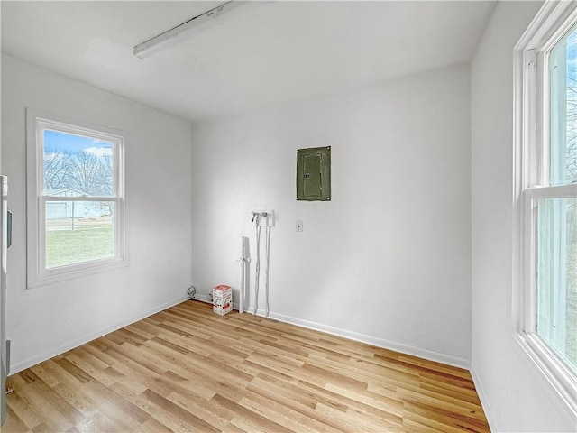 spare room with electric panel, baseboards, and light wood-type flooring