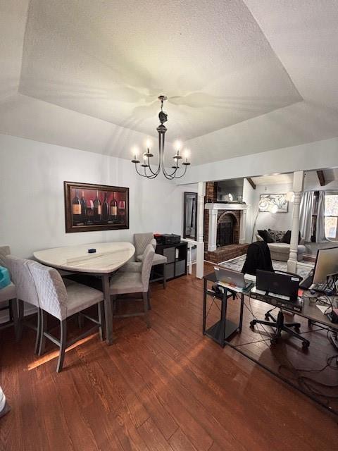 dining space featuring dark hardwood / wood-style flooring, a notable chandelier, a fireplace, and a raised ceiling