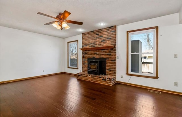 unfurnished living room featuring a ceiling fan, visible vents, baseboards, a wood stove, and hardwood / wood-style flooring