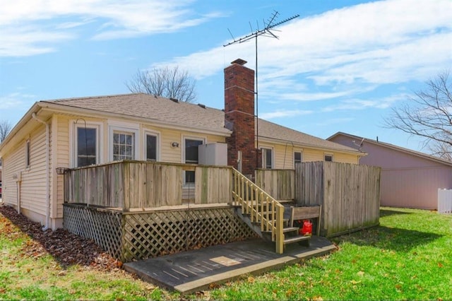 back of property with a wooden deck, a yard, a chimney, and a shingled roof