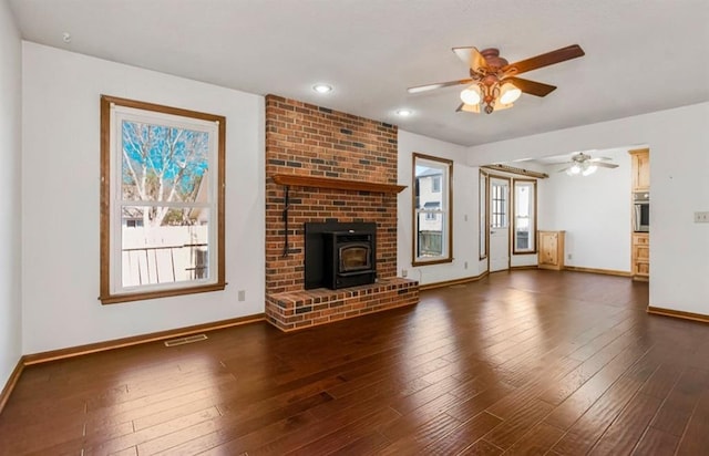 unfurnished living room with a wood stove, baseboards, hardwood / wood-style floors, and a ceiling fan