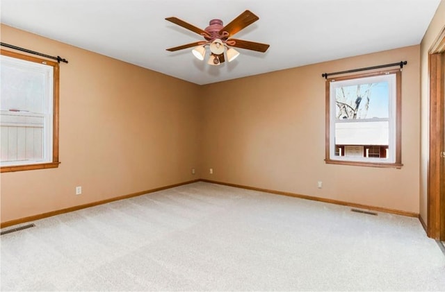 spare room with light colored carpet, baseboards, visible vents, and ceiling fan