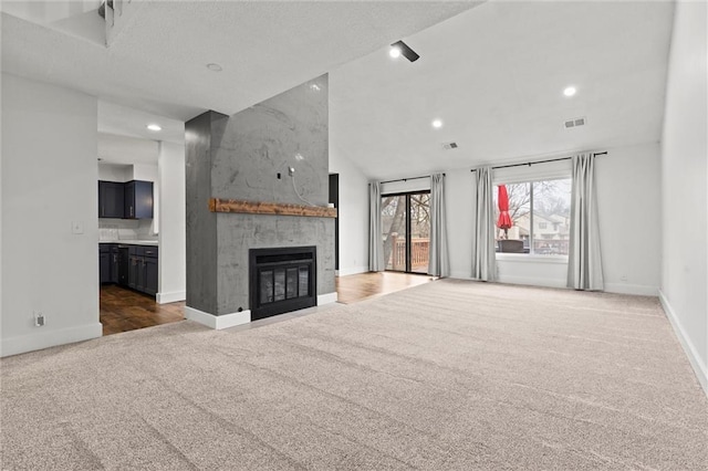 unfurnished living room featuring lofted ceiling, a large fireplace, and dark carpet