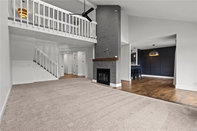 unfurnished living room featuring ceiling fan, a large fireplace, carpet flooring, and high vaulted ceiling