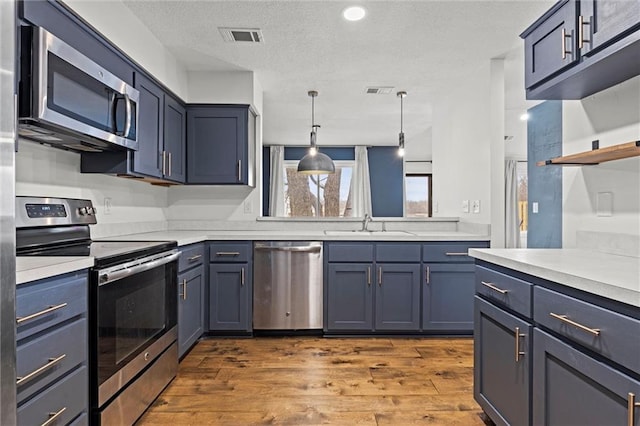 kitchen featuring stainless steel appliances, blue cabinetry, dark hardwood / wood-style flooring, and decorative light fixtures