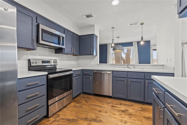 kitchen featuring sink, hanging light fixtures, stainless steel appliances, dark wood-type flooring, and a textured ceiling