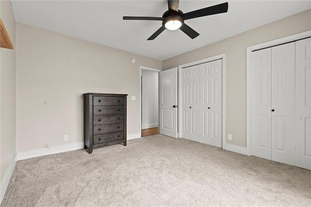 unfurnished bedroom with ceiling fan, light carpet, and two closets