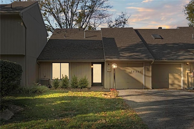 view of front of property with a front yard, driveway, a shingled roof, a garage, and central air condition unit