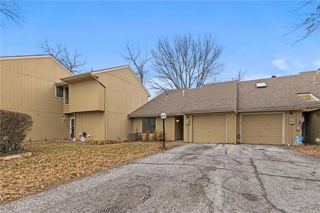 view of front facade featuring aphalt driveway, central air condition unit, an attached garage, and roof with shingles