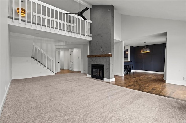 unfurnished living room with wood finished floors, stairway, carpet flooring, a fireplace, and baseboards