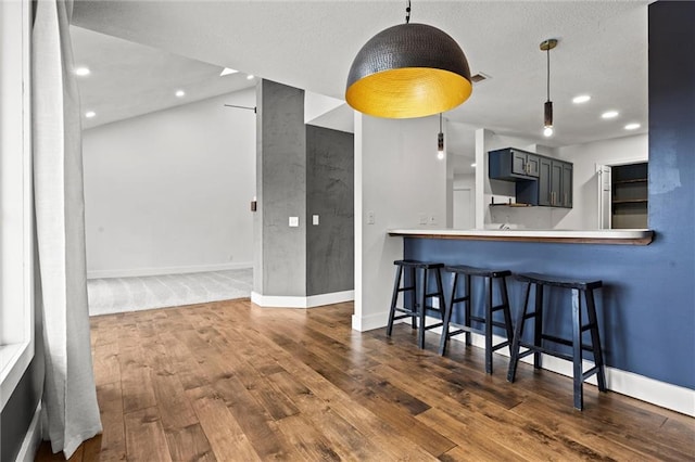 kitchen featuring recessed lighting, a kitchen bar, baseboards, and dark wood-style flooring