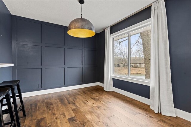 unfurnished dining area featuring a decorative wall, wood finished floors, and baseboards