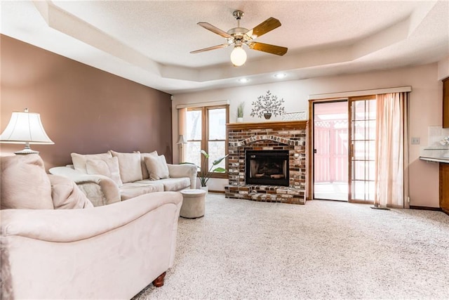 carpeted living area with baseboards, ceiling fan, a fireplace, a textured ceiling, and a raised ceiling