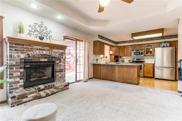 kitchen featuring appliances with stainless steel finishes, a peninsula, brown cabinetry, a raised ceiling, and a brick fireplace