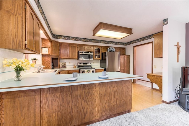 kitchen featuring a sink, appliances with stainless steel finishes, a peninsula, brown cabinetry, and light countertops