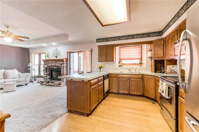 kitchen with brown cabinetry, a peninsula, appliances with stainless steel finishes, a raised ceiling, and open floor plan