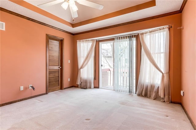 carpeted spare room with ceiling fan, a tray ceiling, baseboards, and ornamental molding