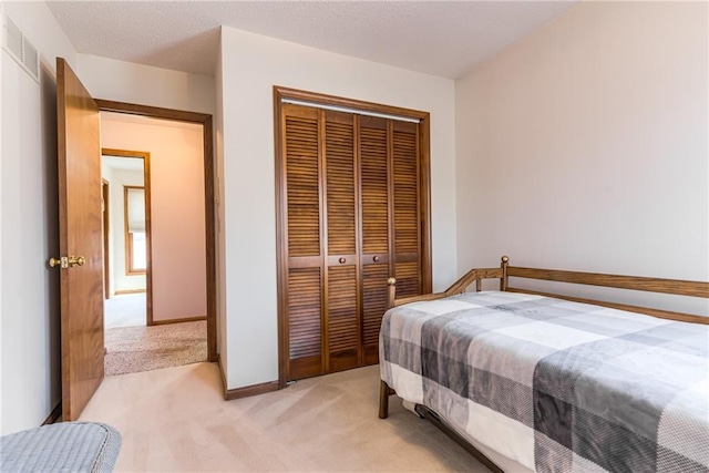 bedroom featuring visible vents, baseboards, a closet, a textured ceiling, and light colored carpet