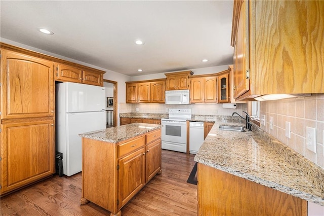 kitchen with white appliances, a sink, a center island, light stone countertops, and backsplash