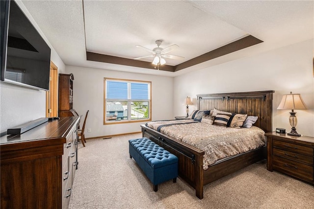 bedroom featuring light carpet, a raised ceiling, baseboards, and a ceiling fan