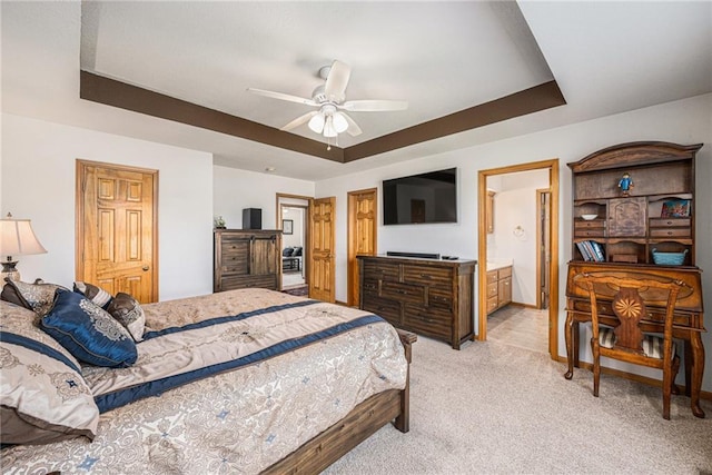 bedroom with a tray ceiling, light carpet, ensuite bath, and ceiling fan