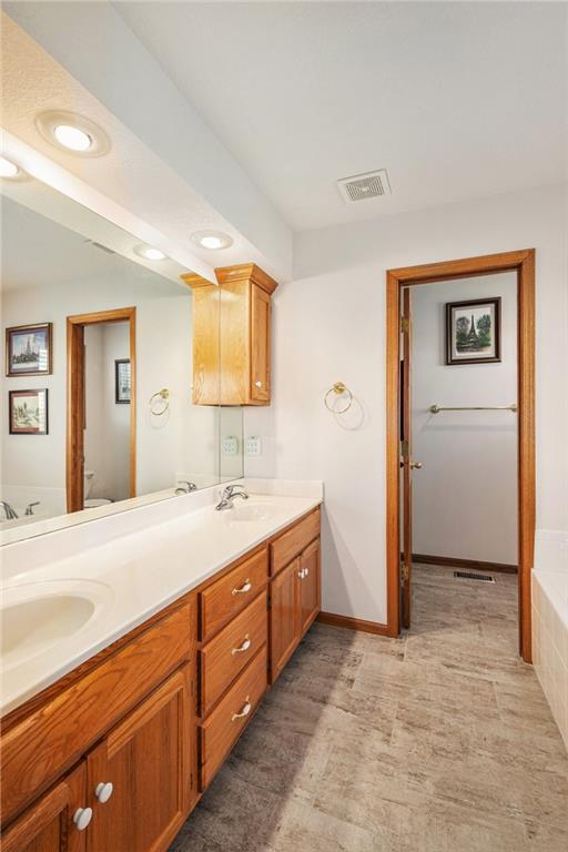 full bathroom featuring recessed lighting, toilet, double vanity, a tub, and baseboards