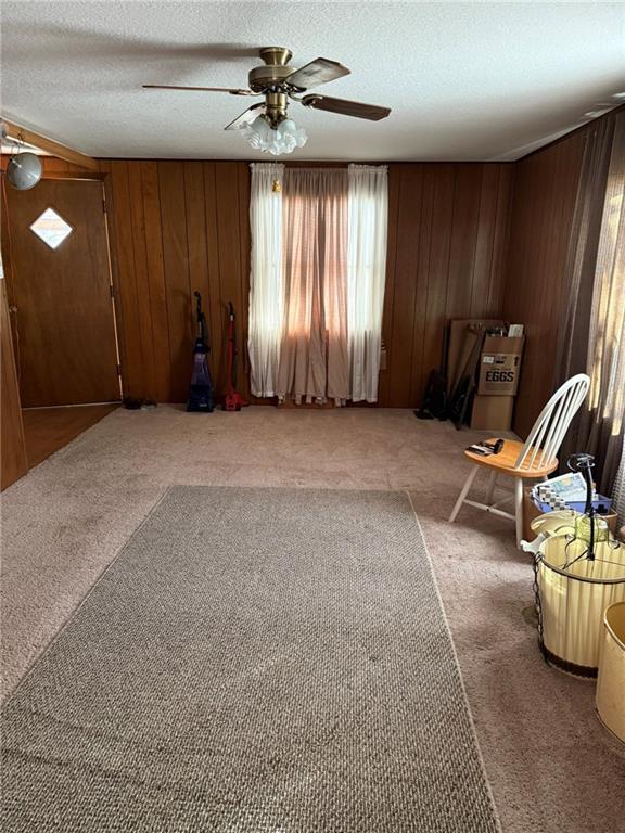 interior space featuring ceiling fan, carpet floors, a textured ceiling, and wood walls