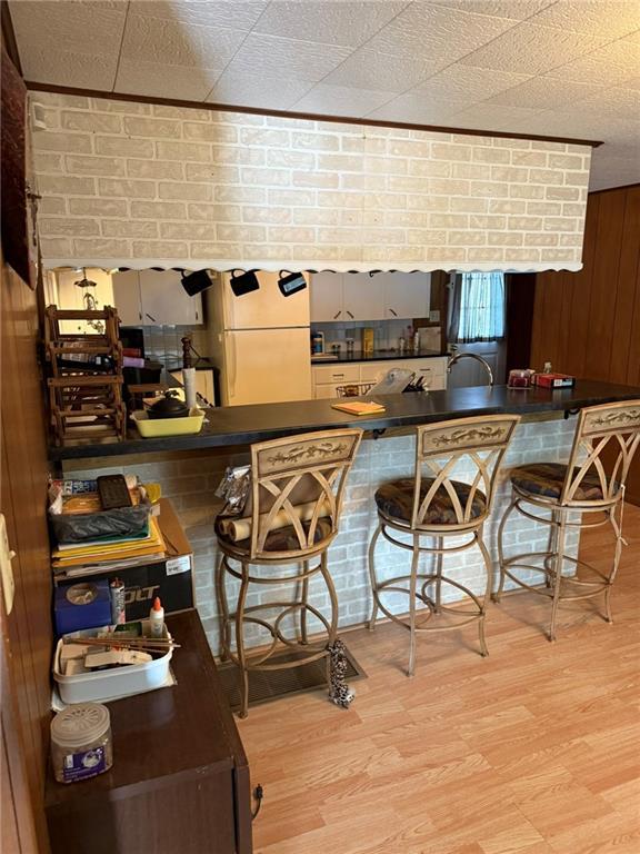 kitchen featuring wood walls, white refrigerator, a kitchen breakfast bar, kitchen peninsula, and light hardwood / wood-style floors