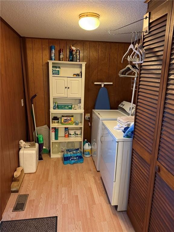 laundry area featuring cabinets, washer and dryer, a textured ceiling, light wood-type flooring, and wood walls