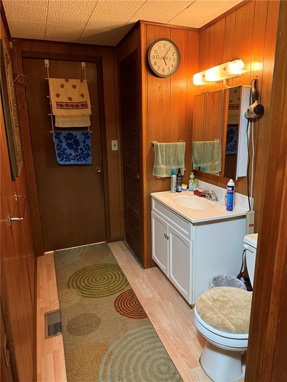 bathroom featuring hardwood / wood-style floors, wooden walls, vanity, a drop ceiling, and toilet