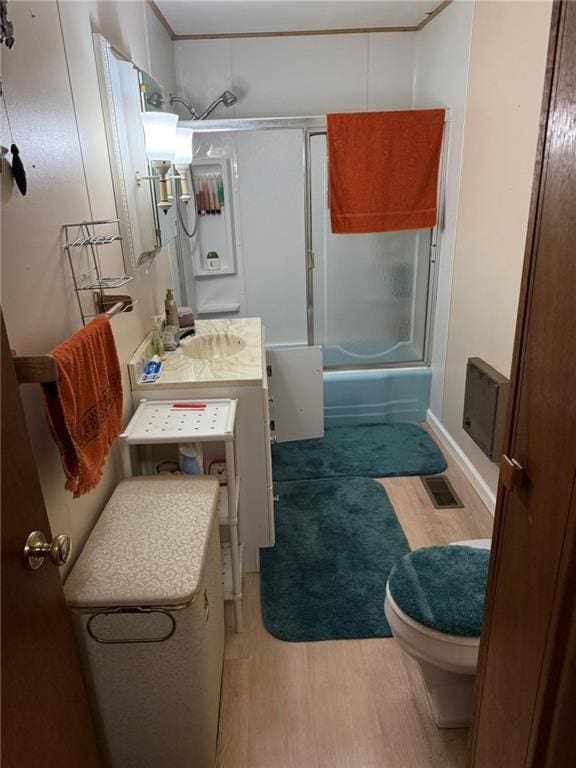 full bathroom with hardwood / wood-style flooring, water heater, combined bath / shower with glass door, vanity, and toilet