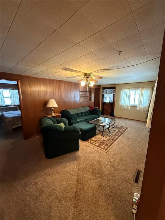 carpeted living room with wooden walls and ceiling fan