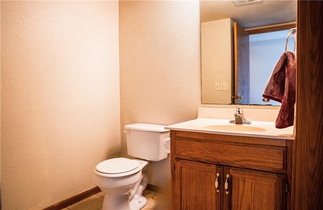 bathroom featuring a textured wall, toilet, vanity, baseboards, and tile patterned floors