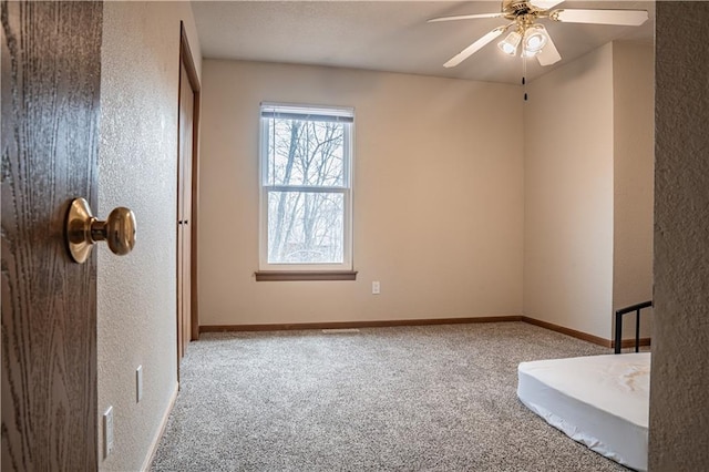 unfurnished bedroom with a textured wall, baseboards, a ceiling fan, and light colored carpet