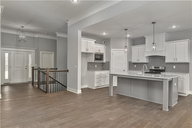 kitchen with white cabinetry, wood-type flooring, appliances with stainless steel finishes, an island with sink, and pendant lighting