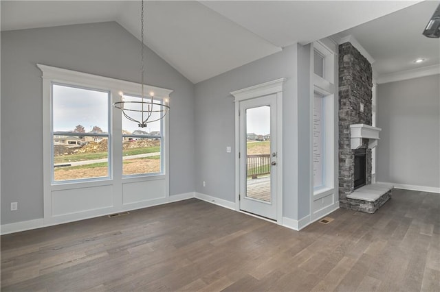 unfurnished dining area featuring dark wood-type flooring, a fireplace, vaulted ceiling, and a notable chandelier