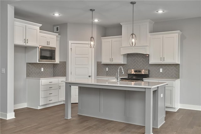 kitchen with a kitchen island with sink, decorative light fixtures, stainless steel appliances, and white cabinets