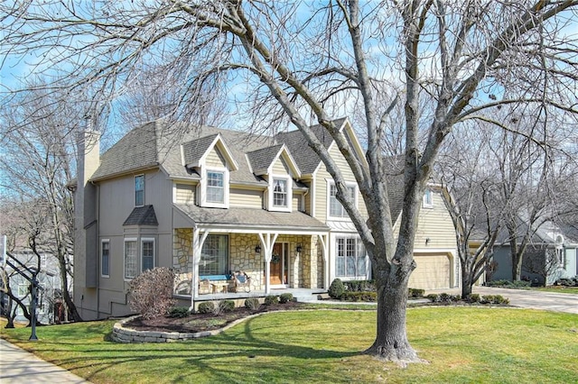 view of front of house with a front yard, covered porch, a chimney, concrete driveway, and stone siding