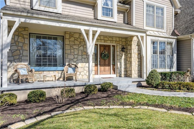 property entrance featuring covered porch, stone siding, and roof with shingles