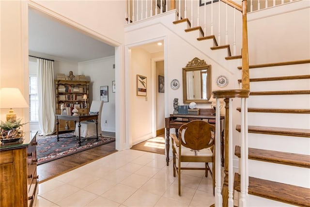 staircase with baseboards, a towering ceiling, crown molding, and tile patterned flooring