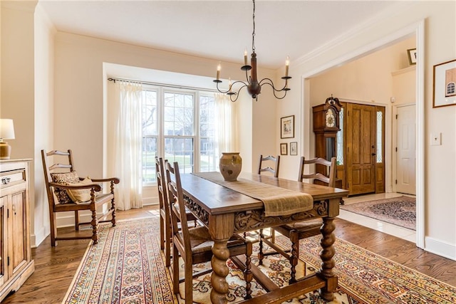 dining space with a notable chandelier, ornamental molding, baseboards, and wood finished floors