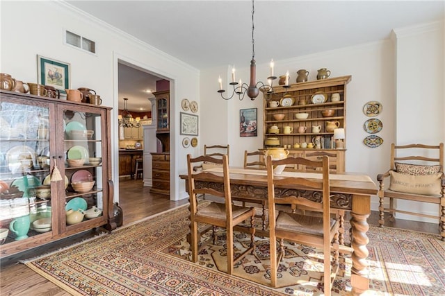 dining room with visible vents, an inviting chandelier, wood finished floors, and ornamental molding