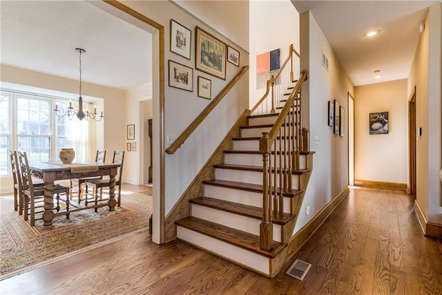 staircase with wood finished floors, visible vents, baseboards, recessed lighting, and a notable chandelier