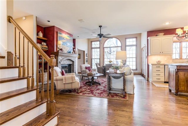 living area featuring stairway, wood finished floors, baseboards, a fireplace, and ceiling fan