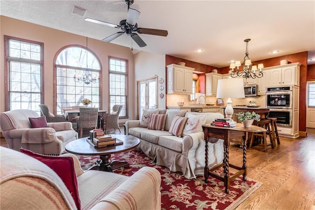 living area featuring ceiling fan with notable chandelier, recessed lighting, light wood-style floors, and a textured ceiling